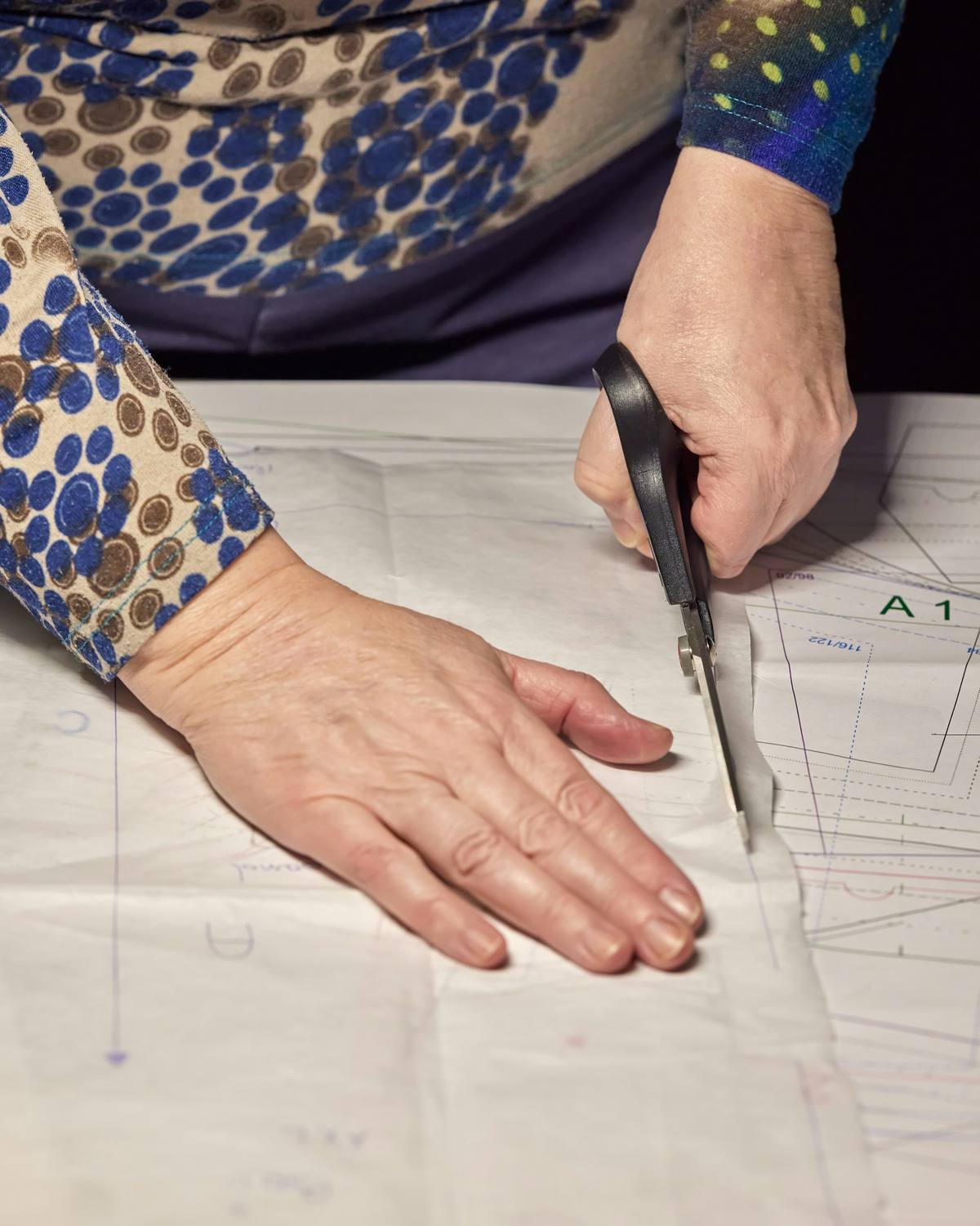 Mains découpant un patron de couture aux ciseaux sur une table
